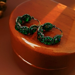 Detail of vintage emerald round earrings with green crystals on dark metal base