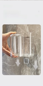 Close-up of clear wall-mounted toothbrush holder with a transparent cup on marble wall