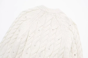 Detail eines weißen Zopfstrickpullovers mit schimmernden Strassstein-Verzierungen