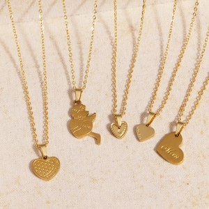 Five gold titanium steel necklaces with heart and angel pendants on beige fabric