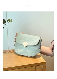 Détail du sac selle vert clair texturé avec boucle coeur dorée et bandoulière chaîne