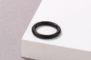 Detail eines glänzend schwarzen Titanrings mit Webstruktur auf geometrischem Block
