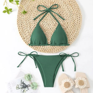 Flat lay of dark green ribbed bikini set with halter top and side-tie bottoms on a straw mat