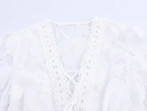 Detail of white V-neck dress with lace texture, scalloped trim and drawstring ties