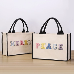 Detail of beige canvas tote bags with Merry and Peace embroidery on a wooden table