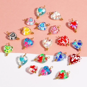 Detailed view of colorful heart-shaped glass pendants with gold loops on pink background
