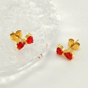 Detailed close-up of bowknot stud earrings with red heart-shaped stones in gold finish