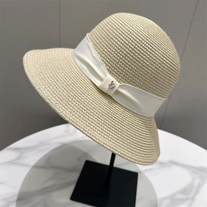 Detail of beige straw hat featuring white satin ribbon and silver metal accent