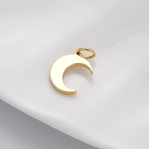 Detail of a crescent moon pendant with gold plating on a clean white ceramic surface