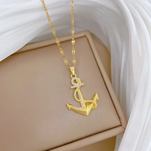 Collier avec pendentif ancre en titane doré et cristaux pavés sur fond de soie blanche