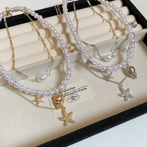 Detailed macro view of starfish and seashell charms on layered gold and silver pearl necklaces