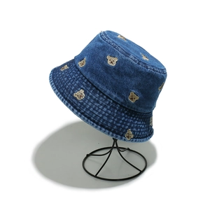 Detail of blue denim bucket hat featuring all-over brown bear embroidery and washed texture