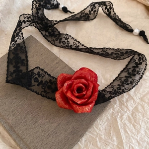 Detailed close-up of a vintage black lace choker with a metallic red rose on a grey book