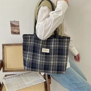 Detail view of plaid tote bag featuring blue and grey woven fabric with brand patch