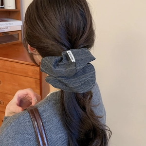 Close-up of a grey herringbone pattern scrunchie with brand tag on a low ponytail hair