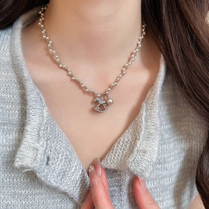 Close-up of pearl necklace with zircon-studded rocking horse pendant on a grey sweater