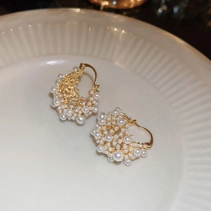 Macro shot of gold-plated hoop earrings with clustered pearls on a ceramic plate