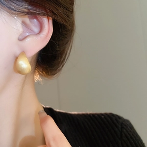 Close-up of gold water drop earrings with matte finish worn by model in a minimalist style