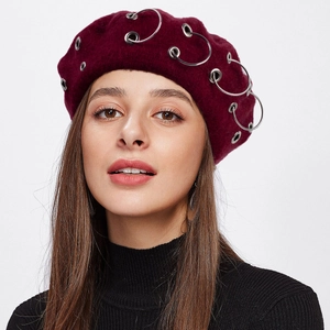 Close-up of wine red wool beret featuring silver metal rings on a model with white background