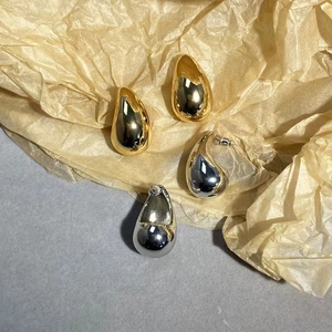 Polished gold and silver teardrop open earrings displayed on a minimalist textured surface