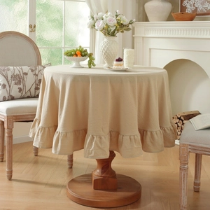 Detail of beige round tablecloth with ruffled hem on wooden table in a warm living room