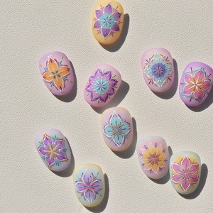 Motifs floraux mandala détaillés sur des faux ongles bohèmes lavande et rose