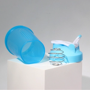 Detail view of a blue protein shaker bottle with measuring scale and metal mixing whisk