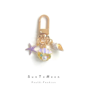 Golden keychain featuring purple starfish, conch, and shell pendant with pearls