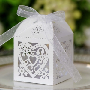 Close-up of white laser-cut heart candy box with elegant organza ribbon on ceramic plate