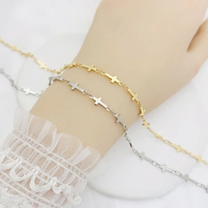 Detailed view of gold and silver cross chain bracelets on a white lace sleeve wrist