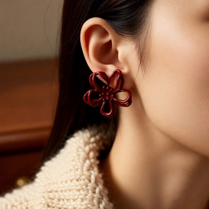 Close-up of red floral earring worn by a model against a warm wooden background
