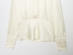 Détail d'un chemisier en satin crème avec des plis à la taille et des zips discrets aux poignets