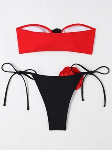 Detail of red bandeau bikini top and black side-tie bottoms with 3D floral accent