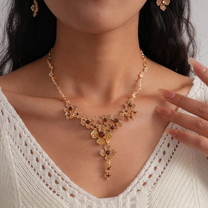 Detail of elegant gold flower necklace with red gems and matching earrings on model
