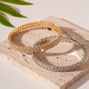 Elegant double-layer rhinestone cuff bracelets and gold bead bangles set on a stone tray