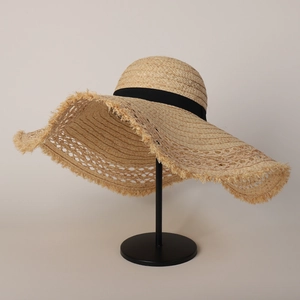 Detail of wide brim straw sun hat featuring frayed edges and black grosgrain ribbon