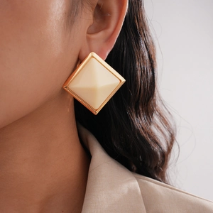 Detail of retro geometric gold metal resin earring on model wearing beige blazer