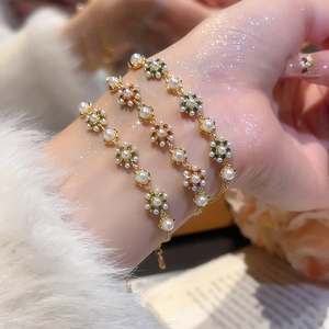 Detailaufnahme von drei goldenen Perlenarmbändern mit bunten Edelsteinblumen am Handgelenk