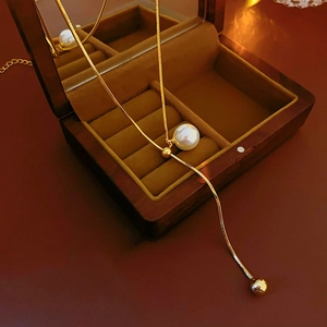 Detail of golden snake chain necklace with round pearl and adjustable slider in a wooden box