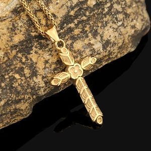 Détail du pendentif croix dorée en acier inoxydable avec gravure florale sur roche naturelle