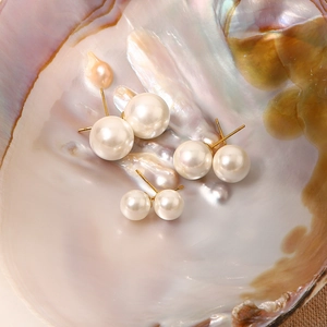 Detailed view of three sizes of round pearl earrings on a shimmering shell background