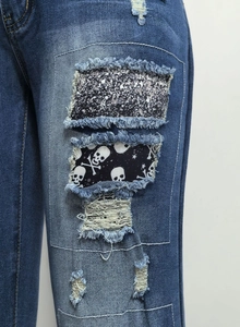 Detailansicht der blauen Jeans mit Totenkopf-Patches und glitzernden Applikationen