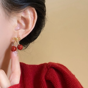 Close-up of red cherry earrings with golden bow detail worn on a model's ear