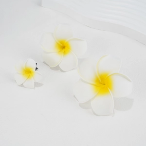 Detailed view of three white and yellow frangipani hair clips on a textured surface