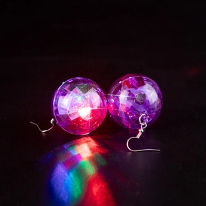 Close-up of glowing purple disco ball earrings with colorful LED light on black reflection