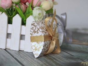 Macro view of white heart-shaped pillow favor box with gold patterns and a satin ribbon