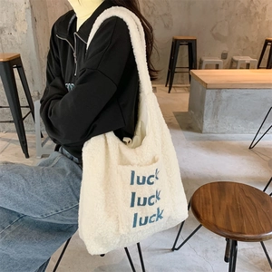 Detail der weißen Plüsch-Tragetasche mit blauer Luck-Stickerei und weicher Textur