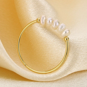 Dettaglio di cinque perle bianche su un anello in acciaio al titanio dorato su raso