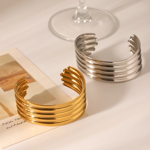 Close-up of layered 18K gold and silver stainless steel open bangles on a glass base