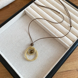 Detail of tiger eye stone diamond pendant with gold textured rings on black jewelry tray